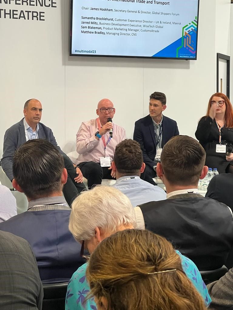 Sam Blakeman on the Multimodal 2023 Digitalisation panel, mic in hand, panel lineup slide visible behind.